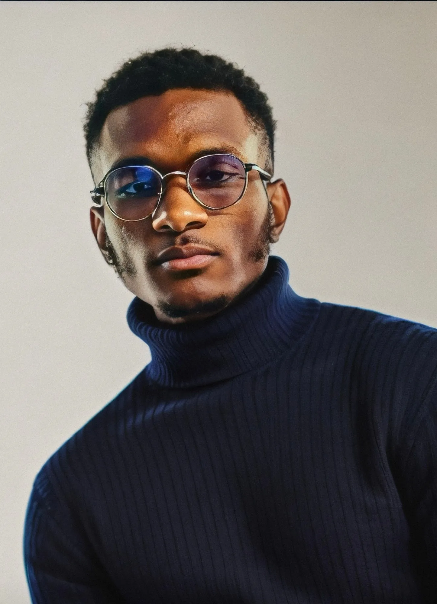 Assane Diallo, wearing round glasses and a navy turtleneck